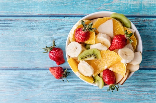Healthy dieting. Fresh fruit salad on blue wooden background top view copy space