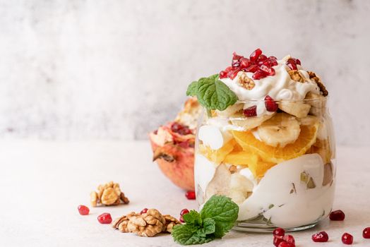 Healthy dieting. Fruit salad with pomegranate, walnuts and fresh fruits in a jar on rustic concrete background front view