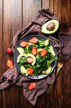 Ketogenic diet. Vegan food. Healthy food concept. Avocado, spinach and strawberry salad top view on wooden background with copy space