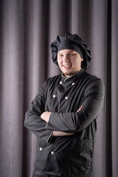 Young smiling Male chef isolated on dark curtain background