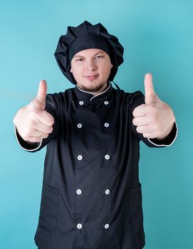 Young smiling male chef showing thumbs up isolated on blue background with copy space