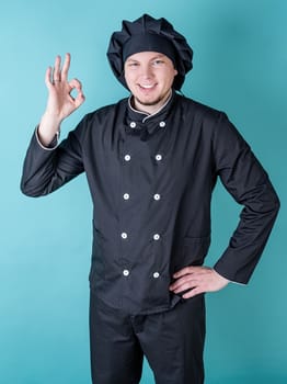 Young smiling male chef showing ok sign isolated on blue background