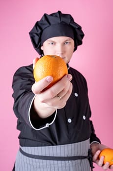 Young smiling male chef holding oranges isolated on pink background with copy space. Selective focus