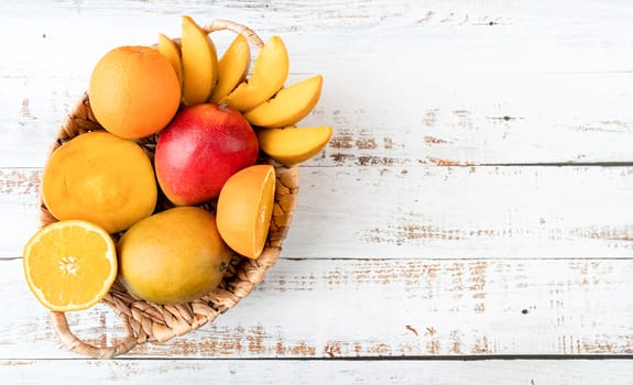 Still life of tropical fruit in basket top view on white wooden background with copy space