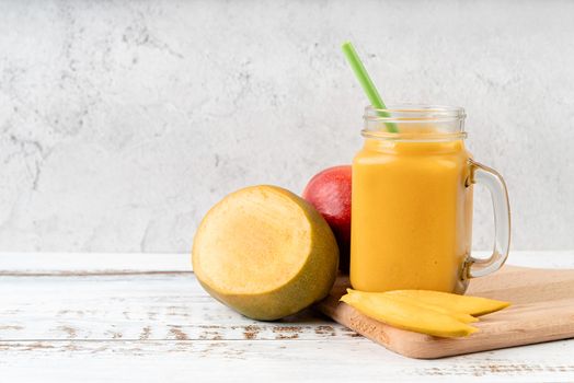 mango smoothie in a mason jar decorated with slices of mango front view on wooden background with copy space