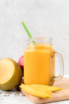 mango shake in a mason jar decorated with slices of mango front view on wooden background
