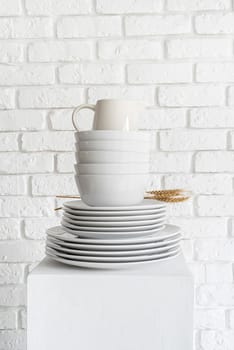 stack of white ceramic dishes and tableware on white brick wall background with copy space