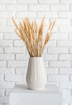 wheat spikes in a white vase as the element of decoration on white brick wall background