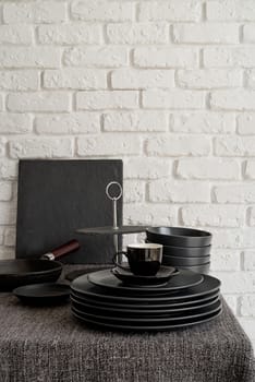 stack of black ceramic dishes and tableware on the table on white brick wall background with copy space