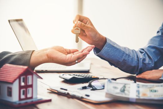 real estate agent gives the keys to the house buyer and signs the contract in the office.