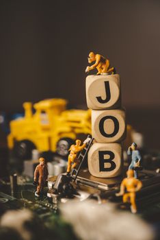 Miniature people or small figure worker on wood block with the word "job". Working for an organization concept.