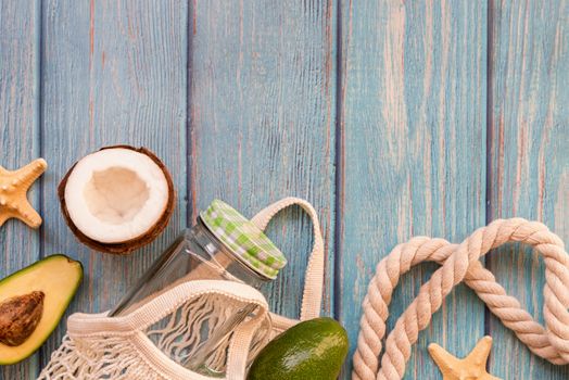 Summer vibes concept. Vacation concept. Mesh bag full of tropical fruit and a mason jar top view flat lay on blue wooden background