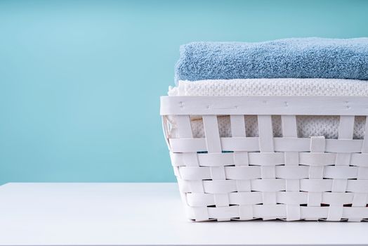 Laundry concept. Stack of clean towels in a white laundry basket isolated on blue background