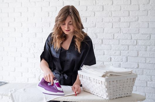Laundry concept. Young beautiful woman in black pajamas ironing at home