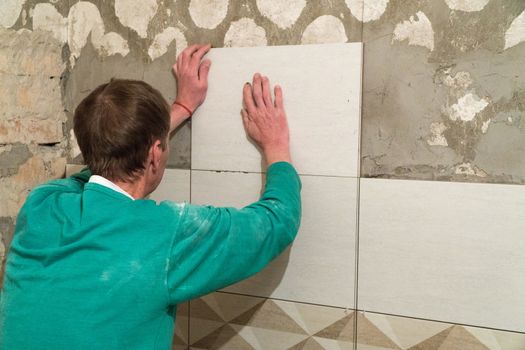 The worker puts tiles on the wall. Finishing works, blurred focus. The technology of laying tile.