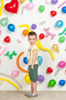 boy on a white background with colorful balloons. boy in a tank top and shorts on a white background with balloons in the shape of a heart