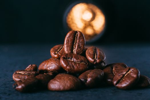 Grains of black coffee on a black granite countertop with yellow light from behind. Advertising photo of coffee.