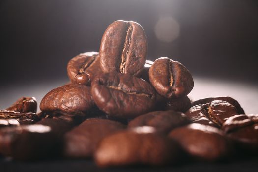 Grains of black coffee on a black granite countertop with yellow light from behind. Advertising photo of coffee. Photo with a glare from the light. Back light on a pyramid with grains.