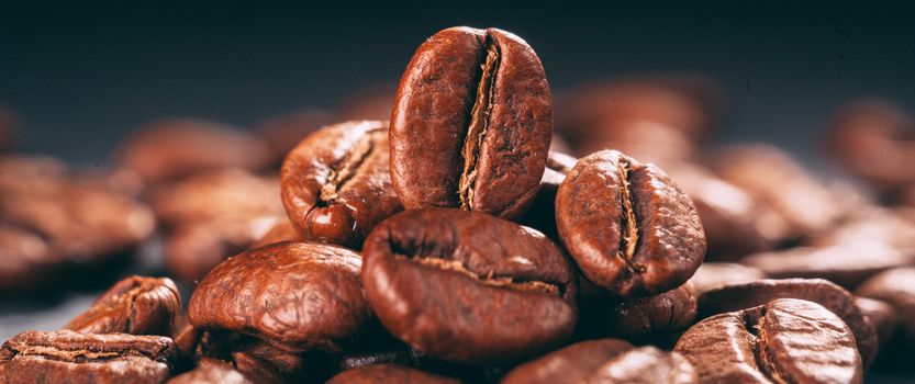 Grains of black coffee on a black granite countertop with yellow light from behind. Advertising photo of coffee. Pour coffee. Macro photo of grains.