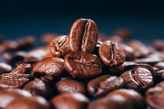 Grains of black coffee on a black granite countertop with yellow light from behind. Advertising photo of coffee. Pour coffee. Macro photo of grains.