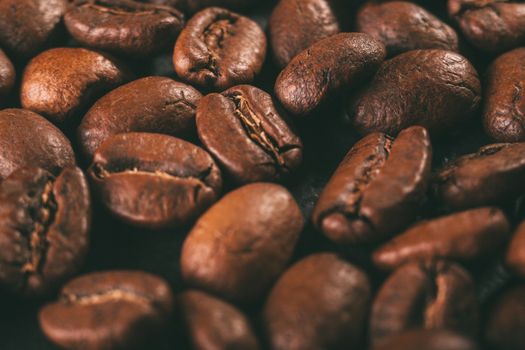 A scattering of coffee beans on a black countertop. The texture of the beans closeup. Vintage style photography.