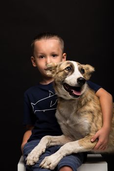 a little boy hugging a dog on a black background. studio shot