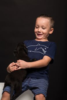 happy little boy hugging puppy on a black background. studio shot