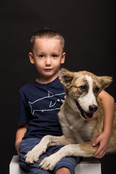 a little boy hugging a dog on a black background. studio shot