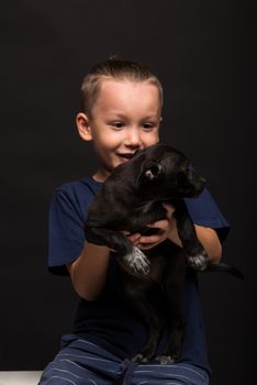 happy a little boy is holding a puppy on a black background. studio shot