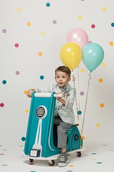 Boy in costume designer on a toy bike with balloons on a white background