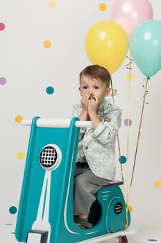 Boy in costume designer on a toy bike with balloons on a white background