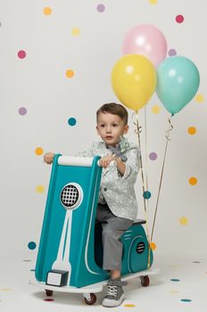 Boy in costume designer on a toy bike with balloons on a white background