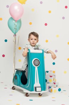 Boy in costume designer on a toy bike with balloons on a white background