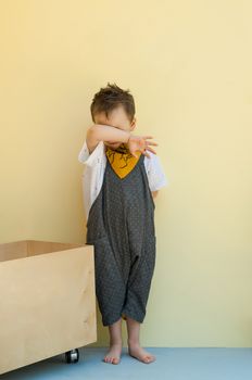 little boy in a jumpsuit with a wooden box on a yellow background