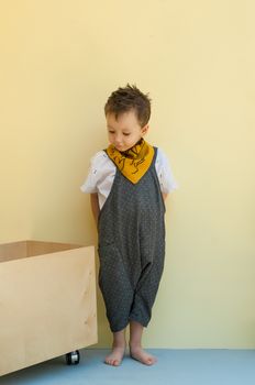 little boy in a jumpsuit with a wooden box on a yellow background