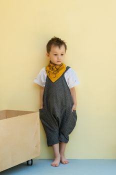 little boy in a jumpsuit with a wooden box on a yellow background