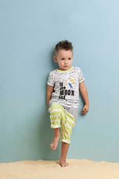 little boy in shorts and t-shirt standing on the sand on a light blue background