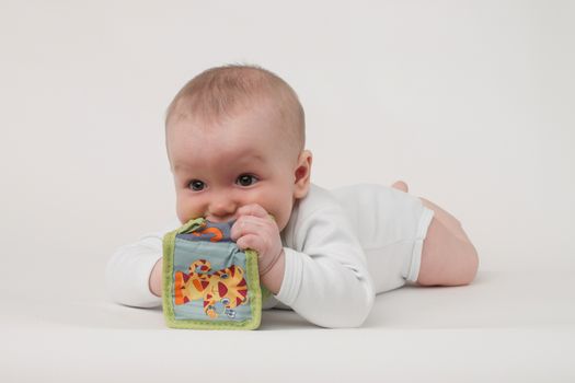 baby on a white background in a white pajamas with toy cube