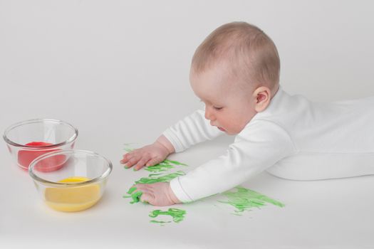 baby on a white background in a white pajamas with paints