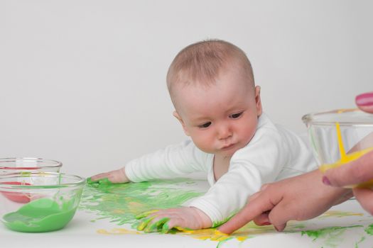 baby on a white background in a white pajamas with paints