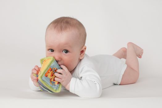 baby on a white background in a white pajamas with toy cube