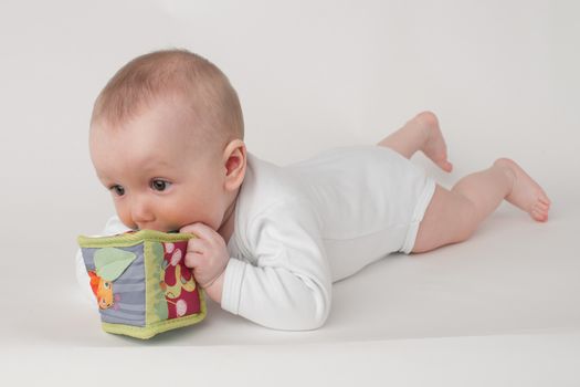 baby on a white background in a white pajamas with toy cube