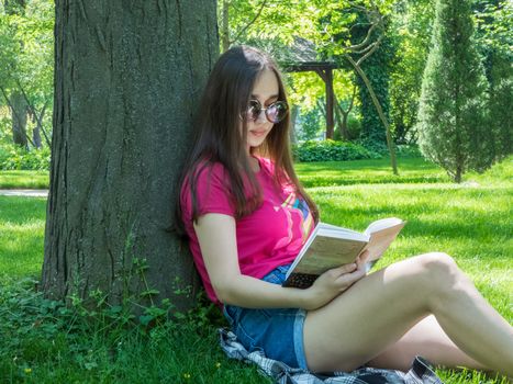 young girl reading a book in a picturesque park, sunny day. the girl of Asian appearance