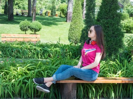 beautiful girl sitting on bench in green park, sunny day. the girl of Asian appearance