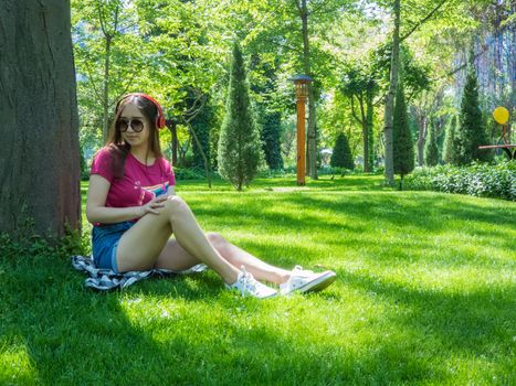 young girl listening to music in a picturesque park, sunny day. the girl of Asian appearance
