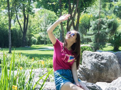 a young girl sitting on a big stone in a picturesque park, hiding from the sun. the girl of Asian appearance