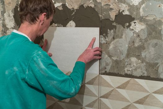 The worker puts tiles on the wall. Finishing works, blurred focus. The technology of laying tile.