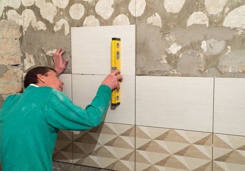 The worker puts tiles on the wall. Finishing works, blurred focus. The technology of laying tile.