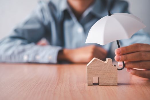 Hands holding an umbrella on a wooden house. Concept of home insurance, home care and safety.