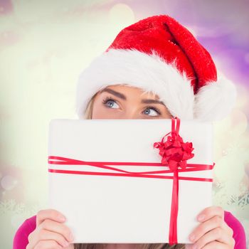 Festive blonde holding christmas gift against glowing christmas background